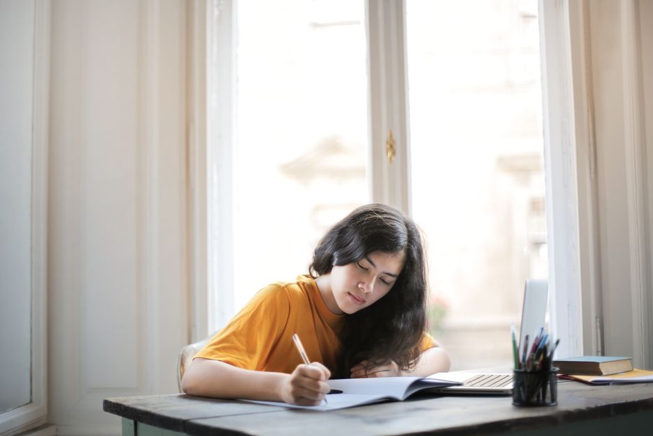 A student writing in a notebook by a window